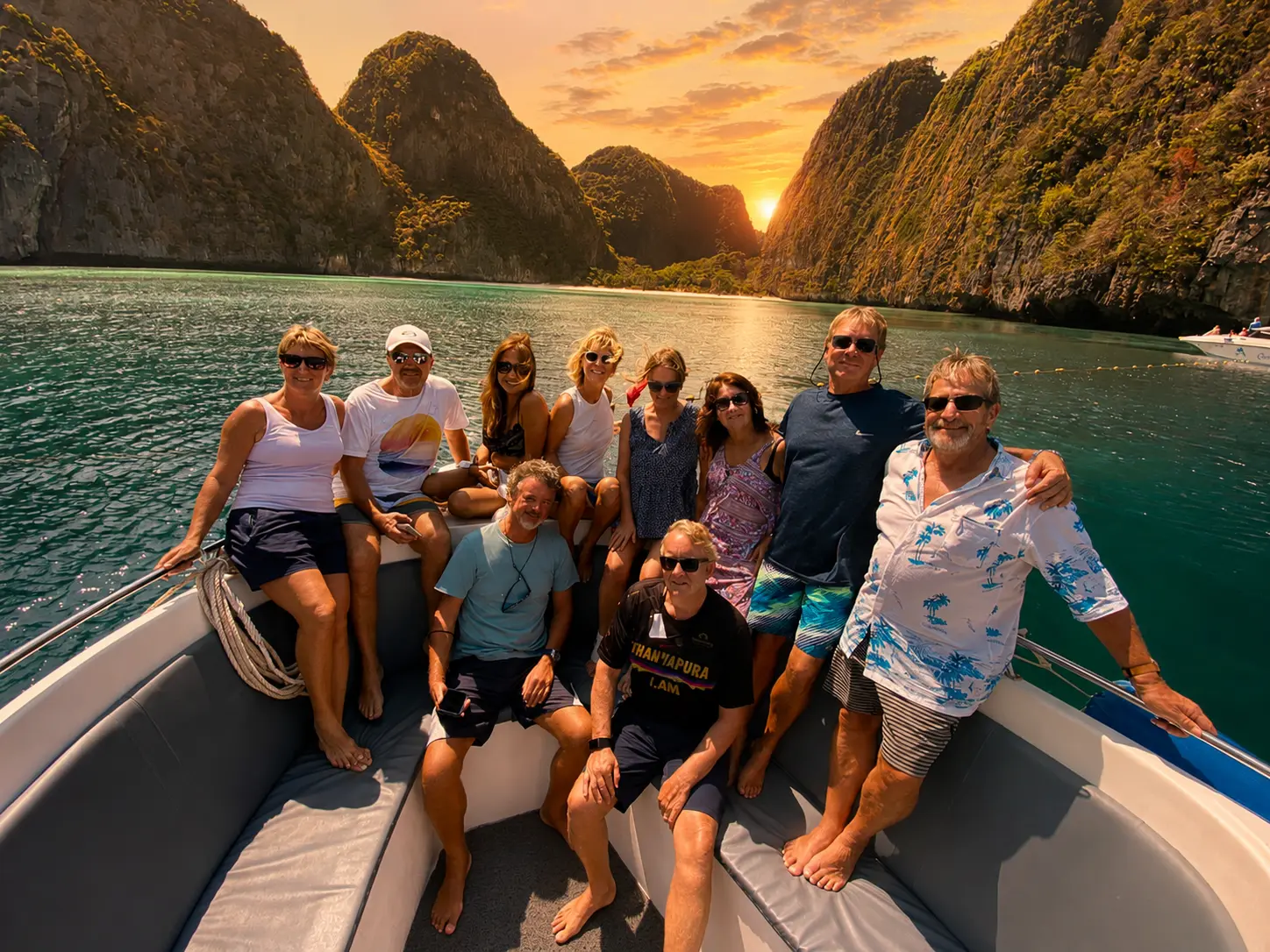 Group of guests posing on the bow of a speedboat between limestone cliffs at sunset in Thailand