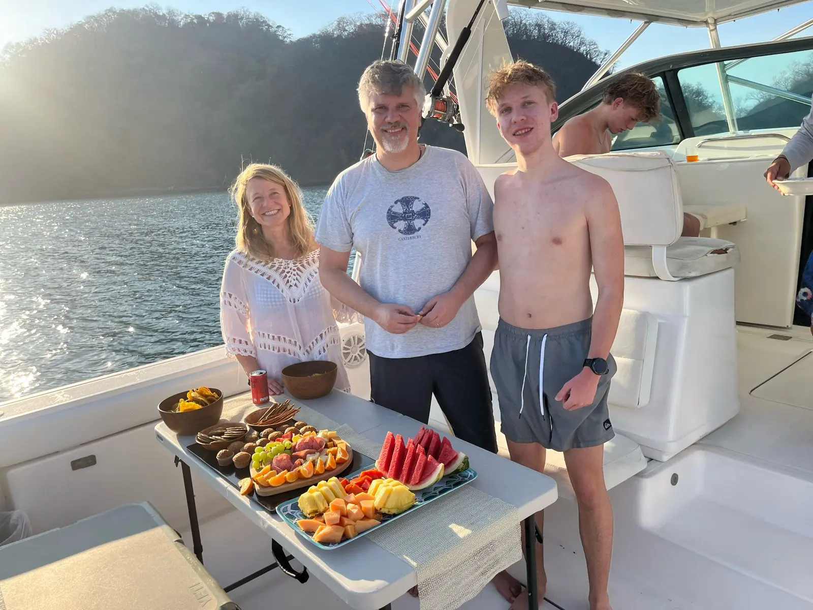 Three guests posing behind a platter of watermelon, pineapple and snacks on the yacht's aft deck