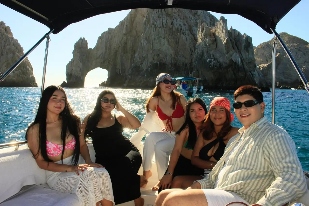 Six guests sit under the small yacht's canopy with the Arch of Cabo San Lucas behind them