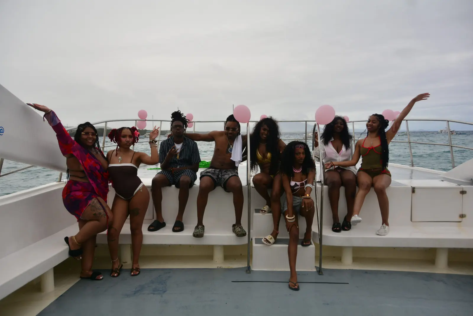 Group of guests posing with pink balloons on the bow of a catamaran under a cloudy sky
