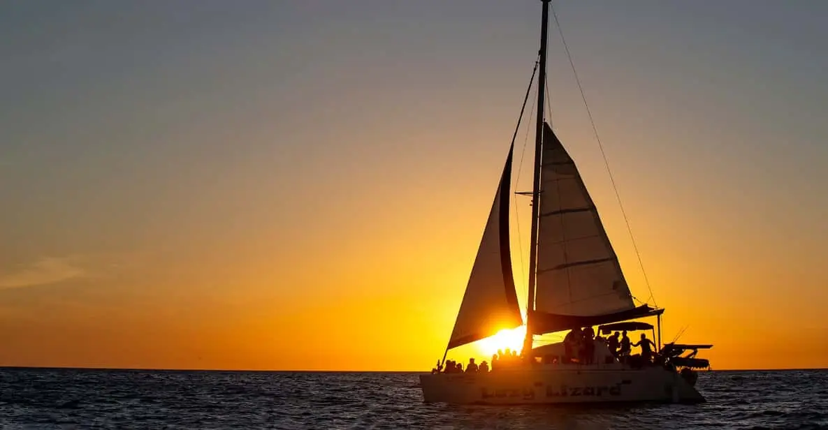 Silhouette of a sailing catamaran under sail as the sun dips to the horizon, guests on deck