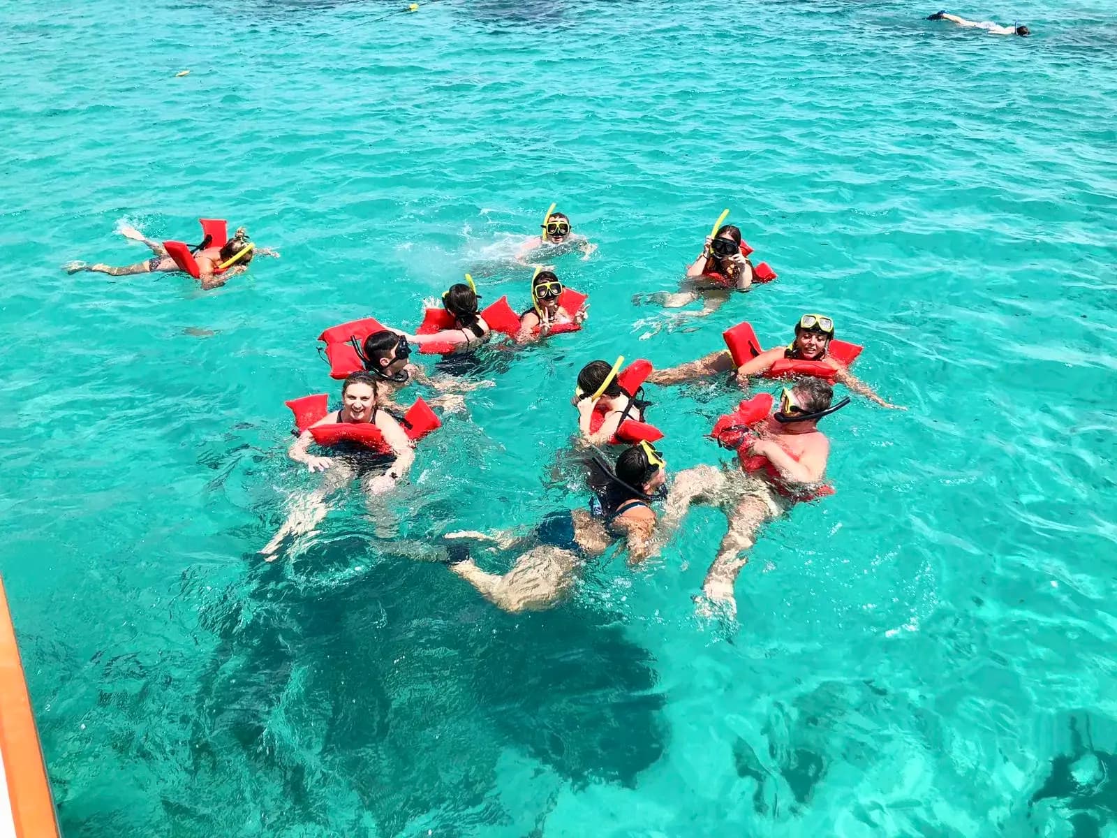 Group of snorkelers in red vests floating over a dark reef patch in turquoise water off Aruba