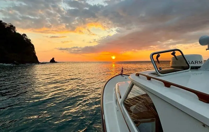 Bow of a motorboat facing the setting sun beside a rocky headland and sea stack in Costa Rica