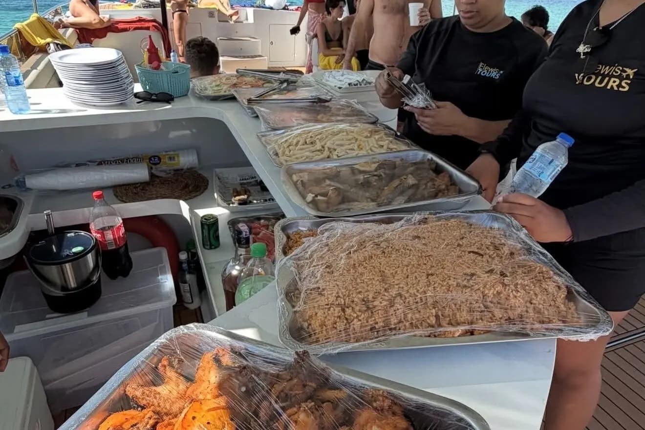 Crew in black T-shirts serving foil trays of fried chicken, rice and pasta aboard a power catamaran