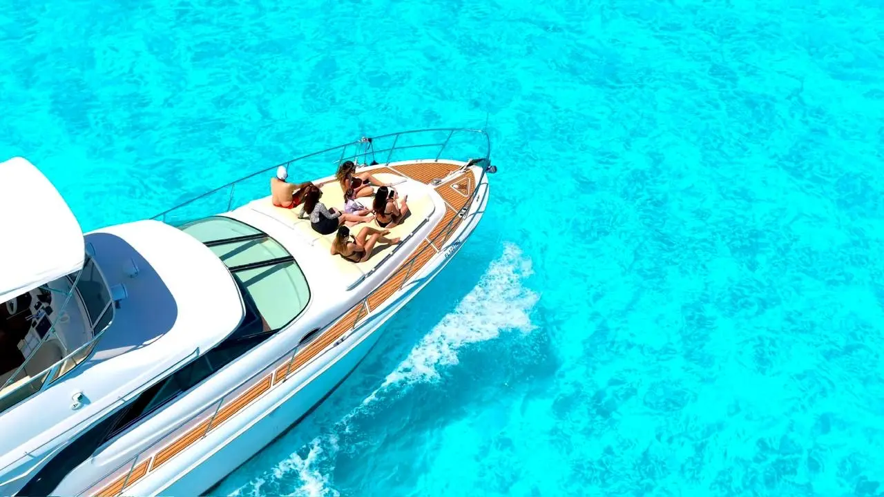 Drone shot of guests sunbathing on the bow of a yacht speeding over turquoise water
