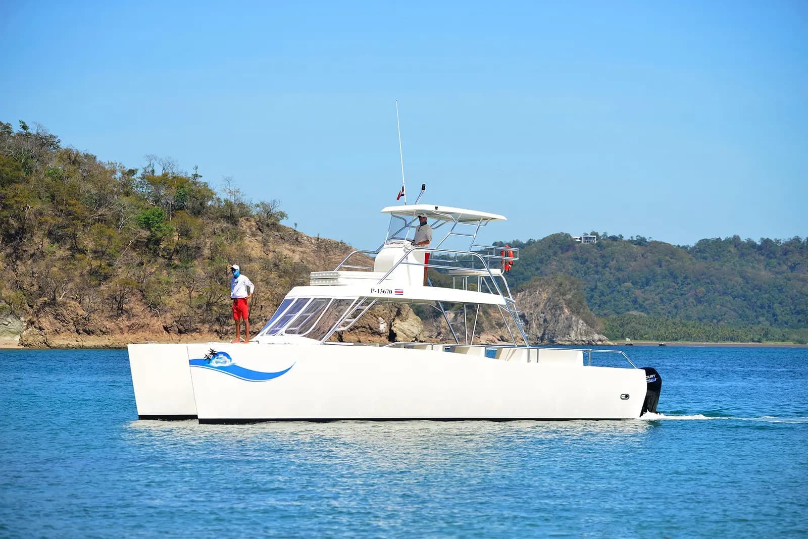 Power catamaran with a flybridge cruising calm blue water below dry forested hills in the Gulf of Nicoya