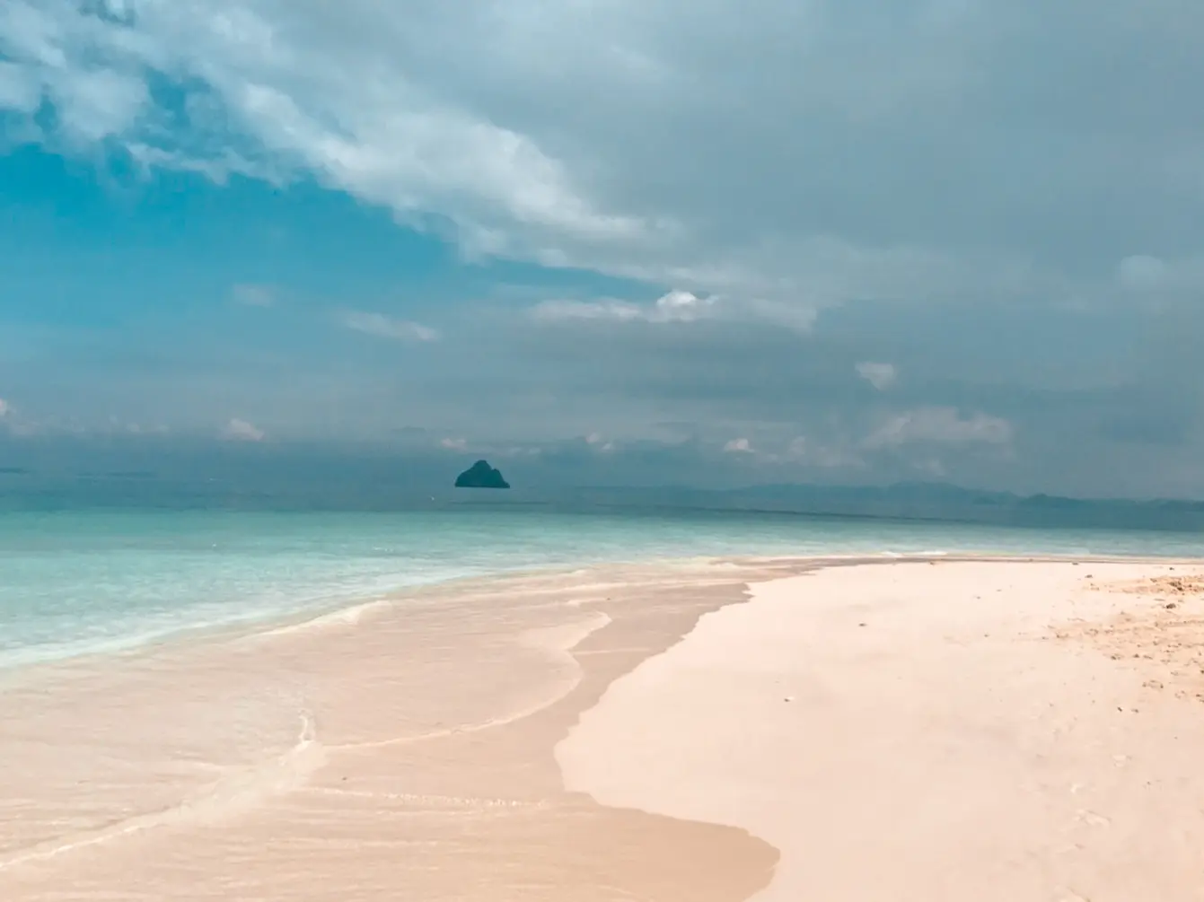 Long white sandbar curving into turquoise water under a cloudy sky at the Khai Islands