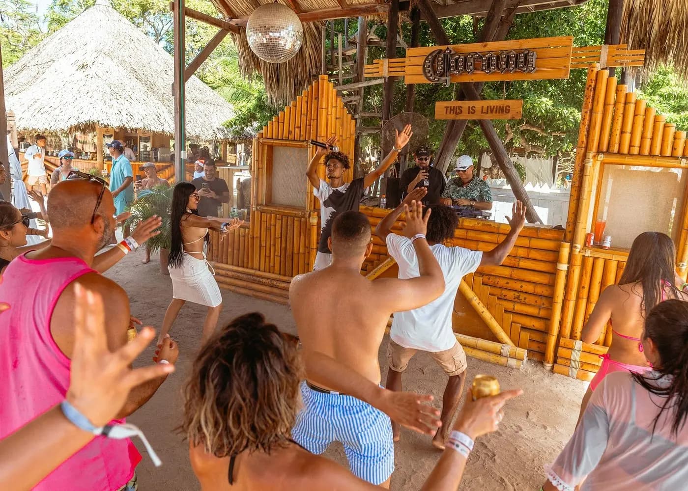 Guests dancing in front of a bamboo bar hung with a disco ball under thatched roofs