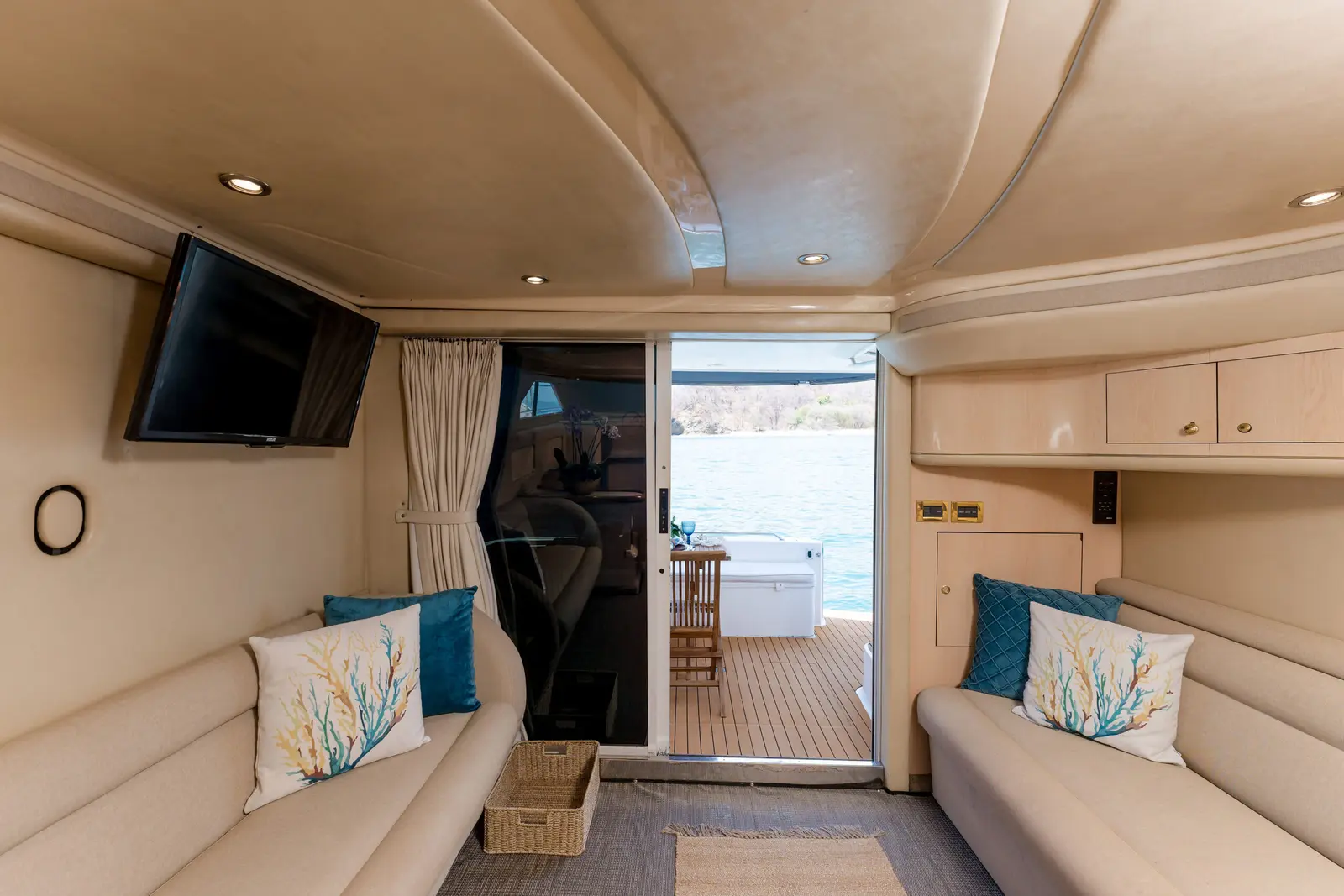Facing cream sofas with coral-print pillows in the yacht salon, leading out to a teak aft deck