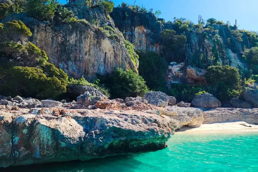 Weathered limestone ledge and green cliffs beside a hidden white-sand beach near Cabo Rojo