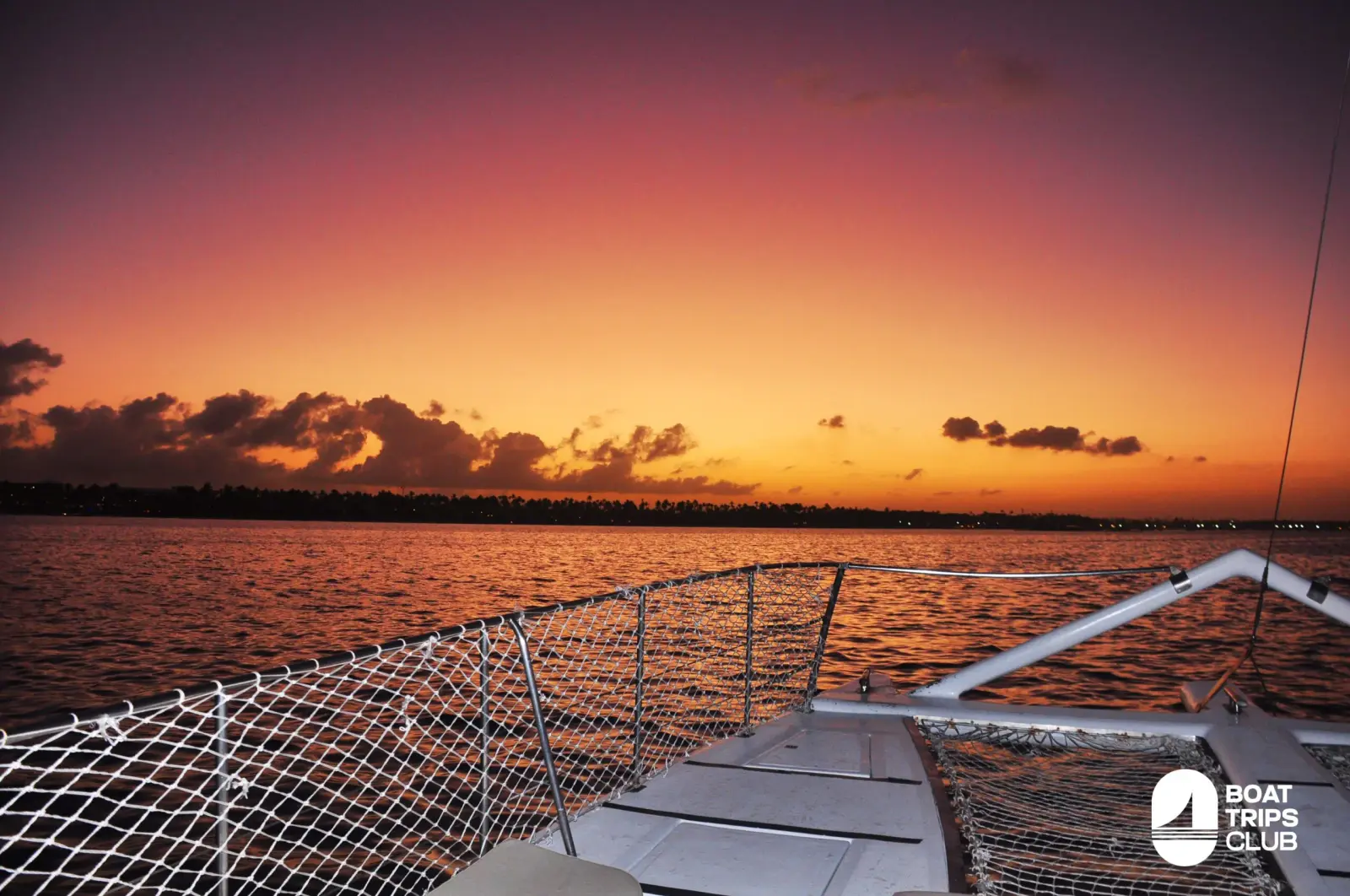 Orange sunset over the Punta Cana coast seen past the netting of a catamaran bow