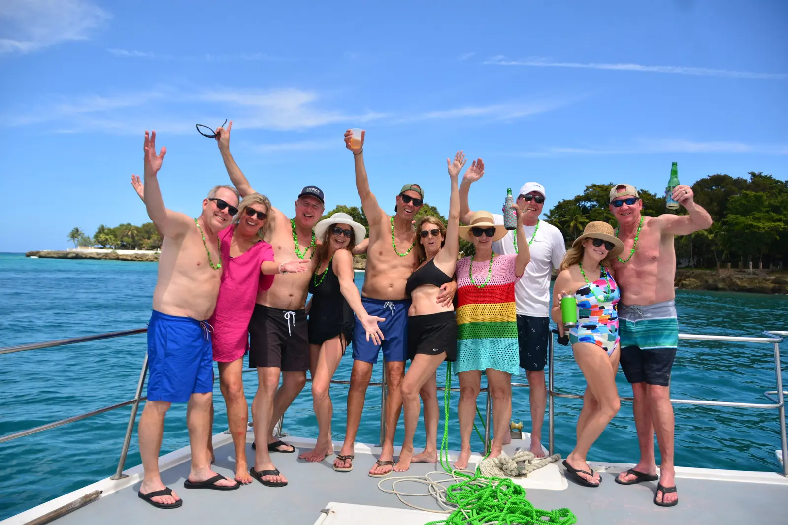 Group of guests cheering with arms raised on a catamaran off Puerto Plata, palm-covered shore behind