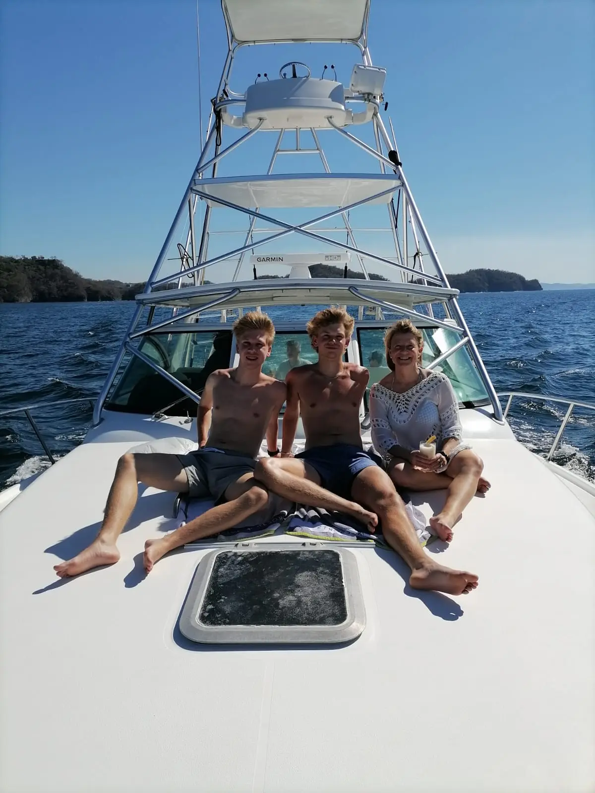 Three guests sitting together on the bow of a sportfishing yacht with the Papagayo coast behind