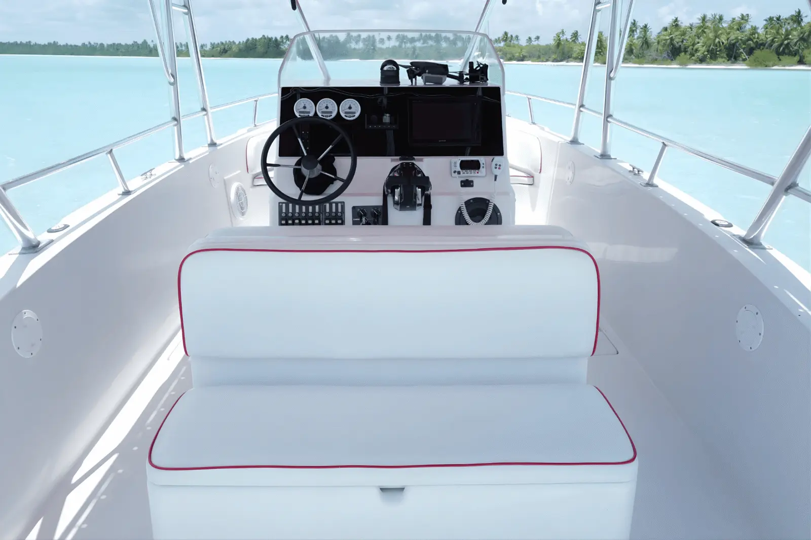 Speedboat helm with steering wheel, gauges and a white seat with red piping, palm-lined shore ahead