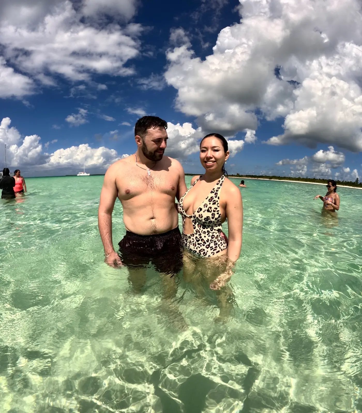 Couple standing in clear knee-deep water off Cozumel under a blue sky with puffy clouds