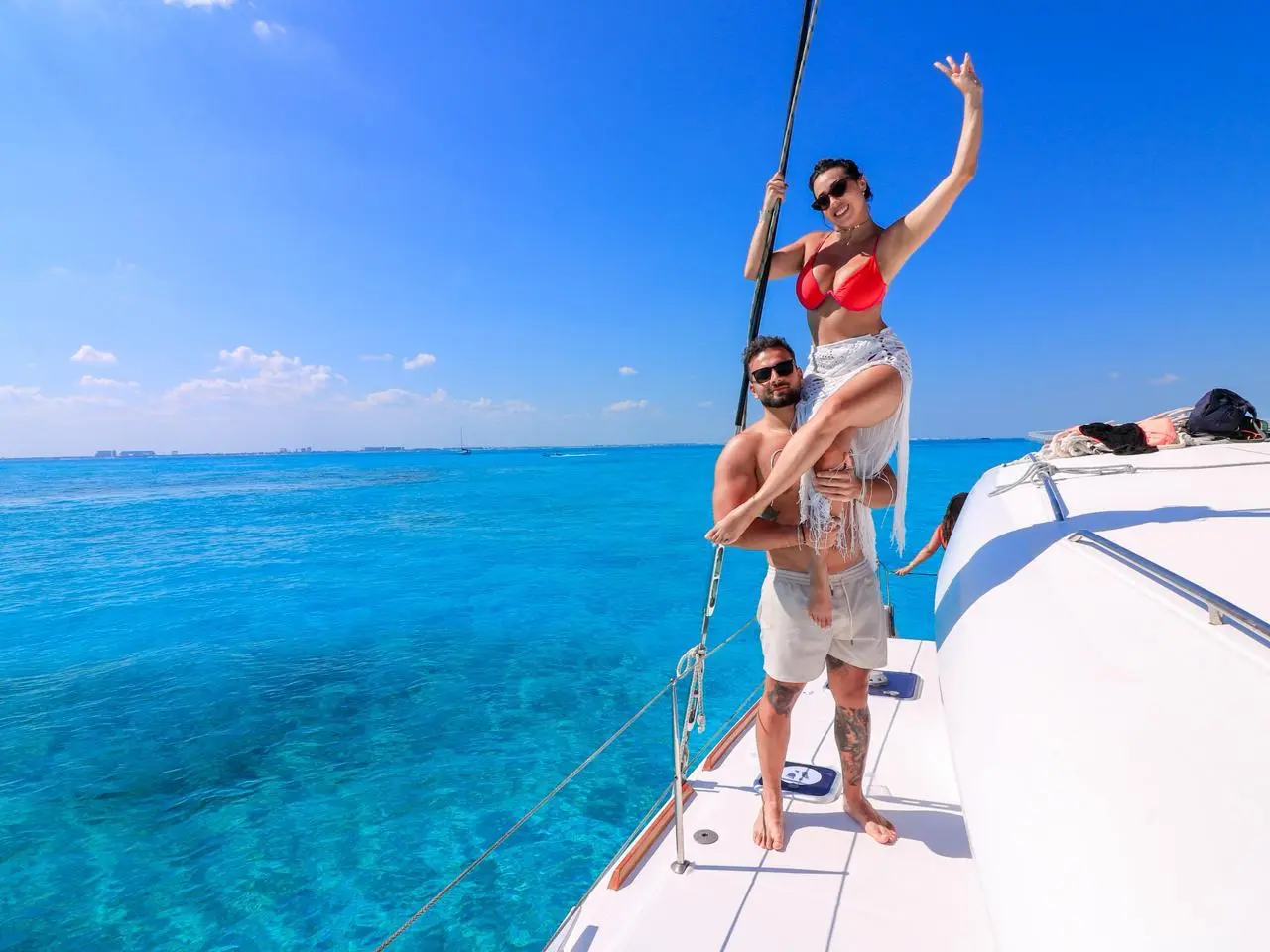 Man lifting a waving woman in a red bikini by the catamaran's rigging off Cancún