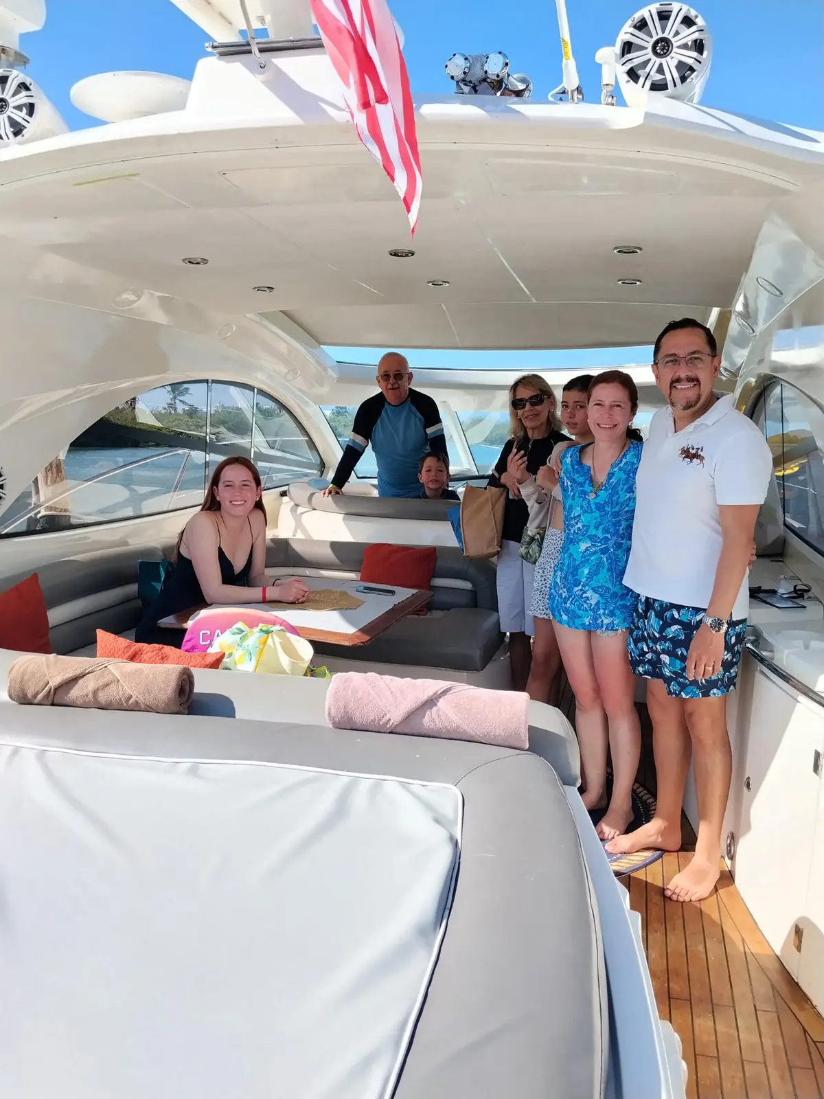 Group of guests smiling in the shaded cockpit of a motor yacht beside its cushioned sun pad