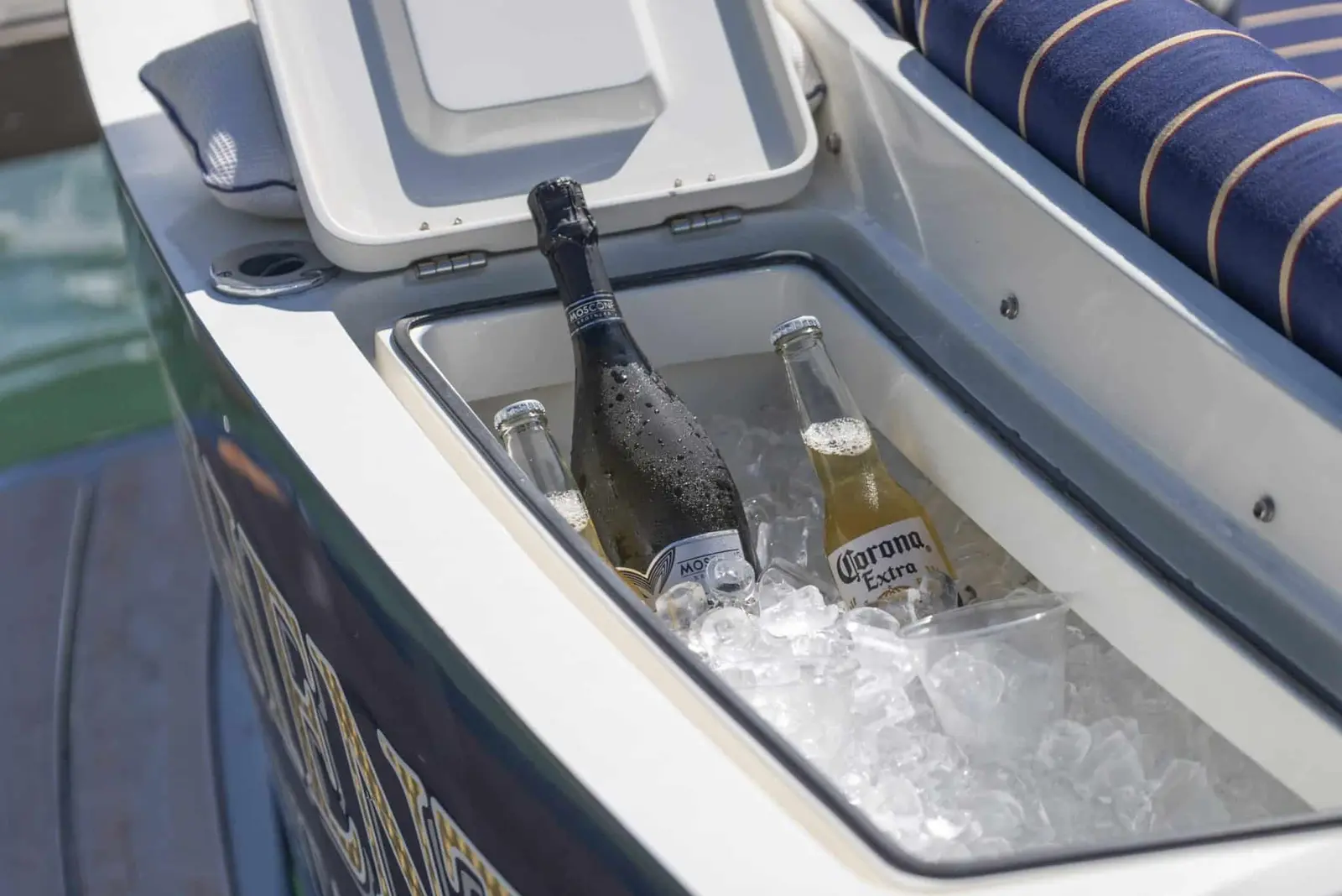 Deck cooler packed with ice, sparkling wine and bottled beer beside striped seat cushions