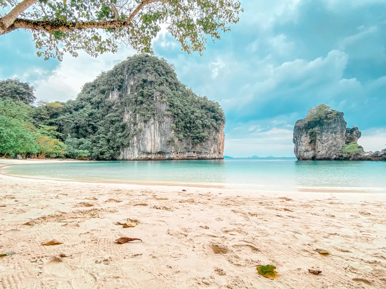 Sandy beach marked with footprints facing a jungle-topped limestone islet and sea stack off Krabi