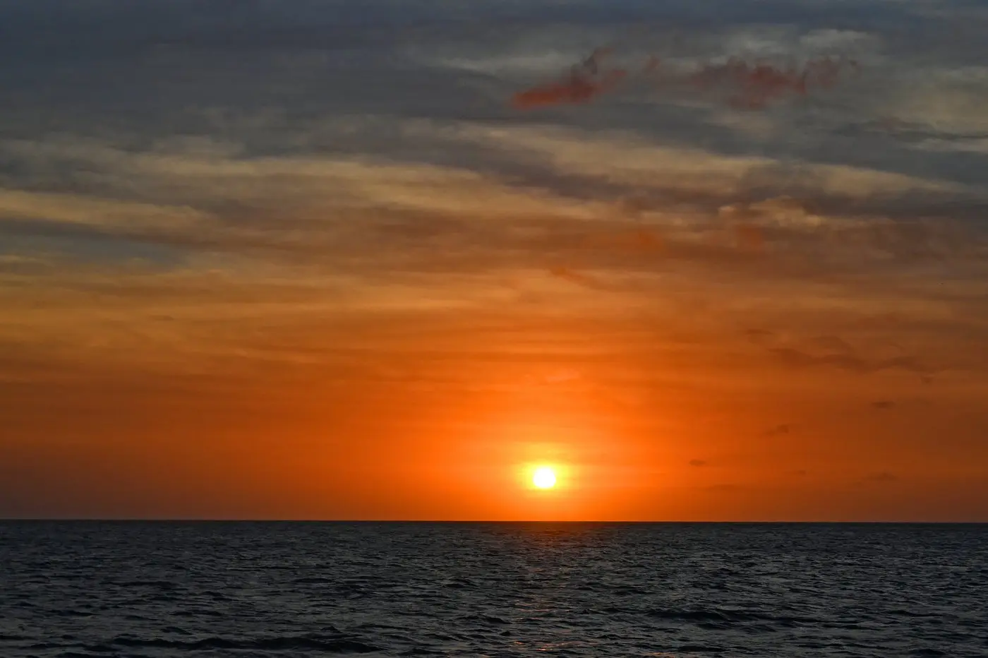 Orange sun sinking toward the horizon under scattered clouds at dusk off Aruba