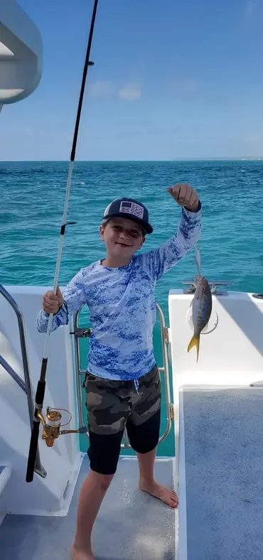 Boy in a cap and sun shirt holding up a small fish on the deck of a fishing boat