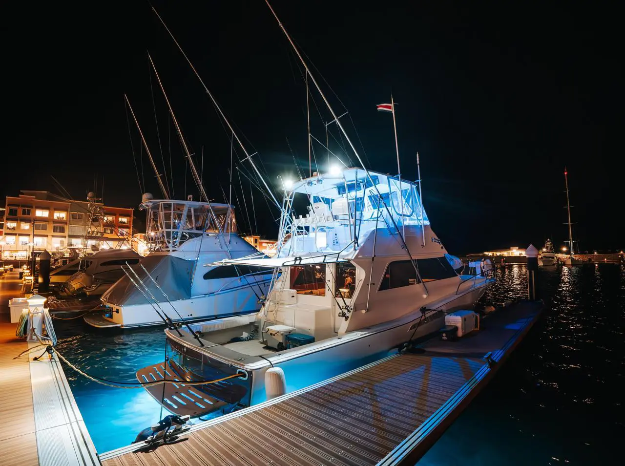 Sportfishing yachts lit up at night in their marina slips beside a glowing Costa Rica waterfront