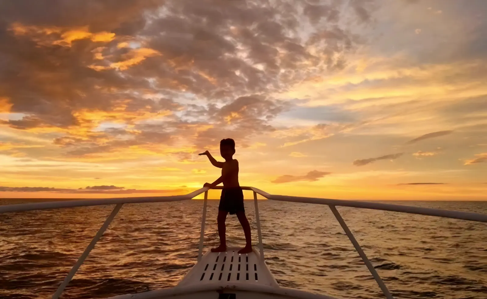 Child silhouetted on the bow of the sportfishing boat against a fiery orange sunset off Costa Rica