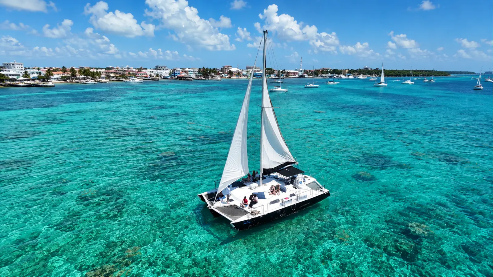Sailing catamaran with guests cruising turquoise reef waters off the Belize coast