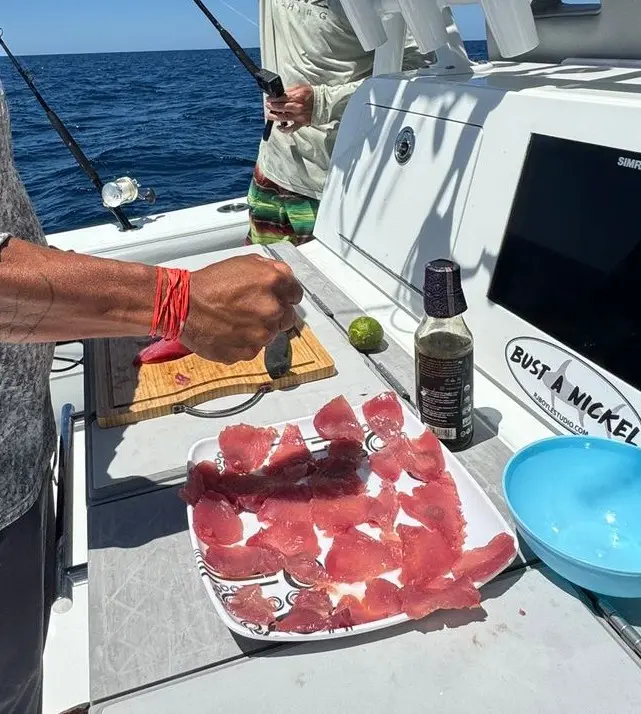 Freshly sliced raw tuna on a plate beside soy sauce and a lime on the boat's counter