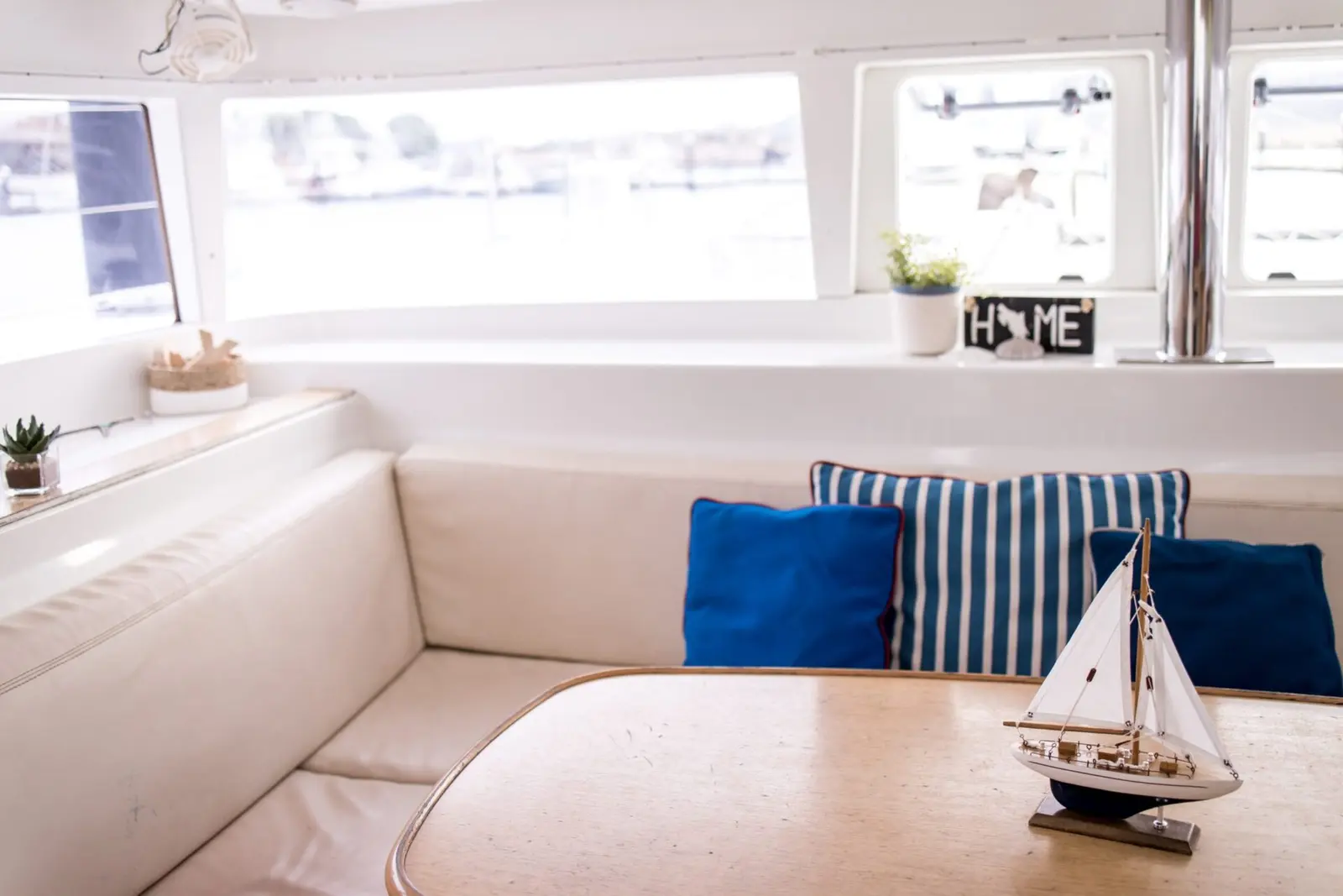 Catamaran saloon with a cream settee, blue striped pillows and a model sailboat on the table