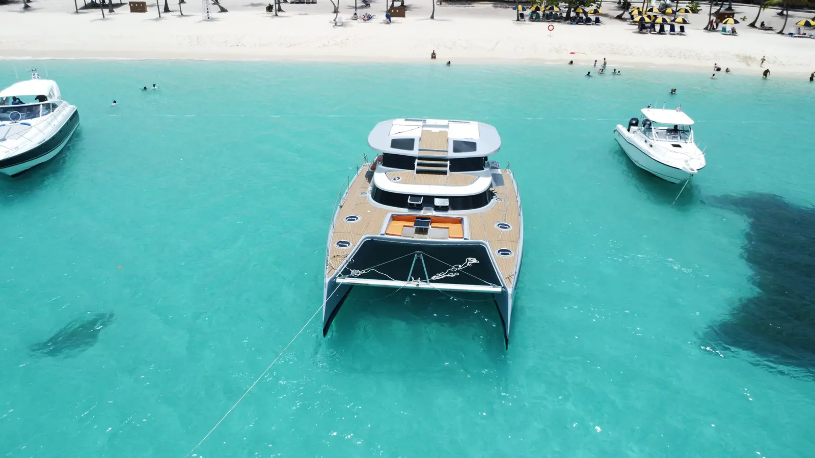 Aerial view of a power catamaran anchored in turquoise shallows off a busy beach in the Dominican Republic
