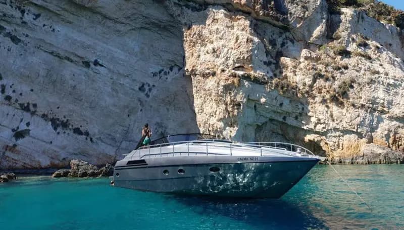 Silver sport yacht anchored in turquoise water beneath white limestone cliffs off Mykonos