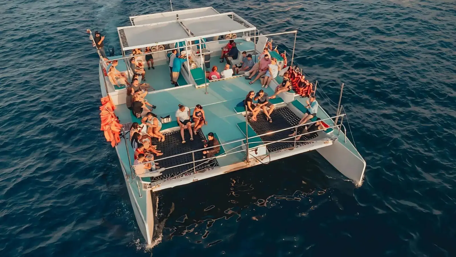 Aerial view of a catamaran deck crowded with guests and orange life vests on the water off Los Cabos