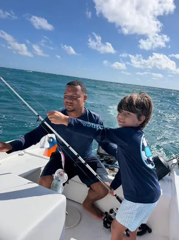 Boy fighting a fish on a bent rod as a crew member helps at the stern