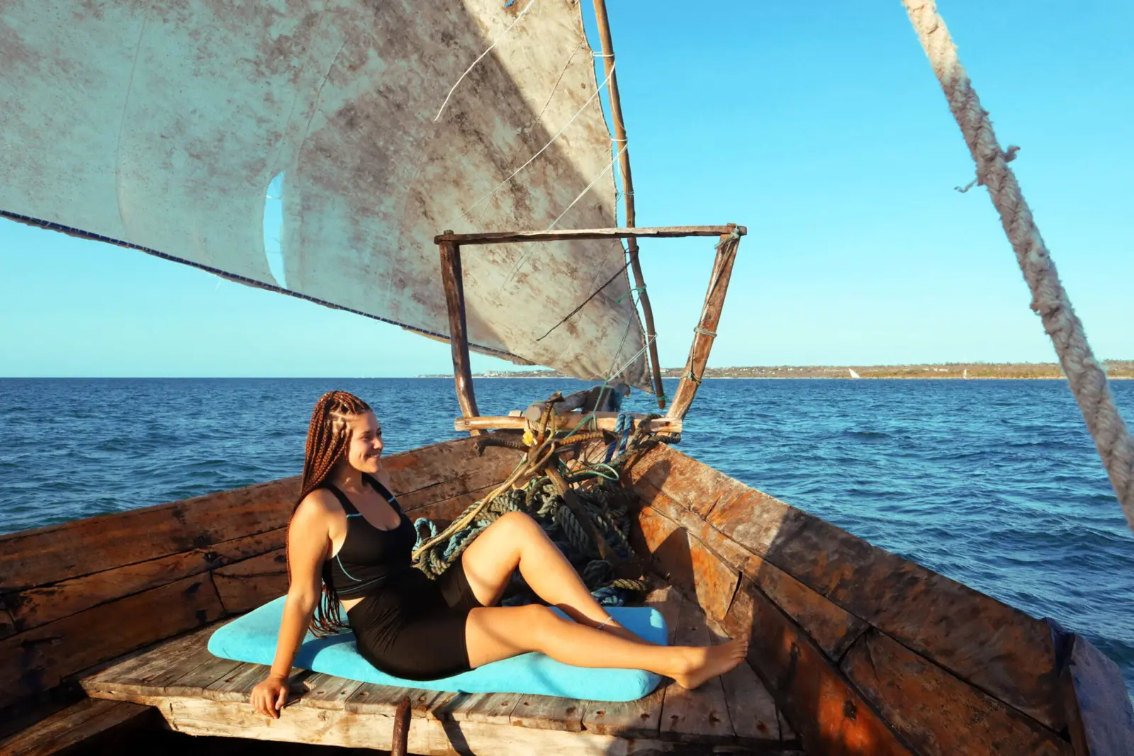 Woman in a black swimsuit relaxing on a cushion at the wooden bow of a dhow under sail off Zanzibar