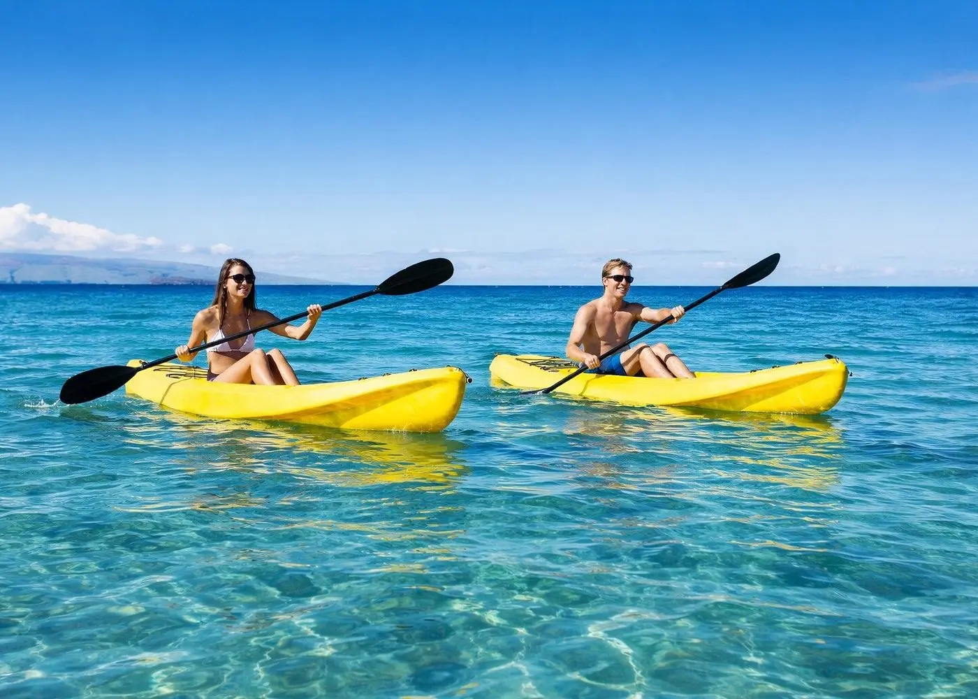 Two guests paddle yellow kayaks across clear shallow water near La Paz