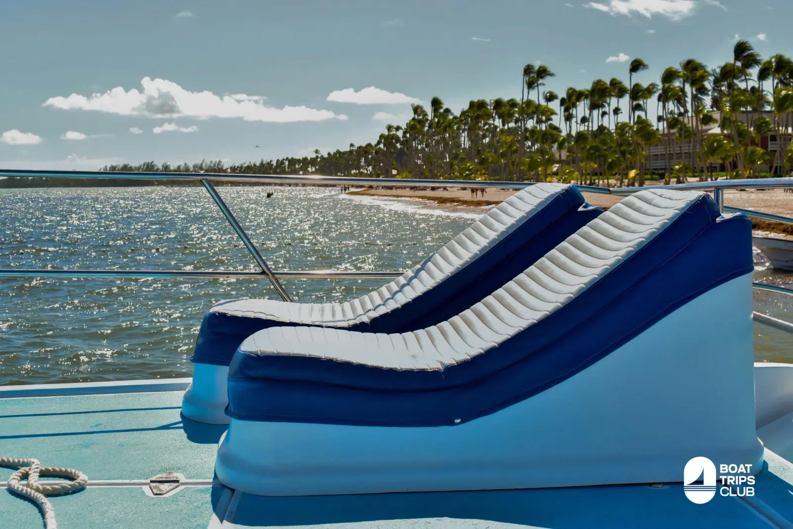 Two blue and white loungers on a catamaran deck overlooking sparkling water and a palm-lined Punta Cana beach