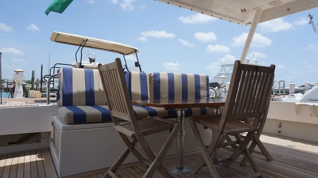 Teak aft deck of the motor yacht with a wooden table, folding chairs and blue-and-white striped cushions