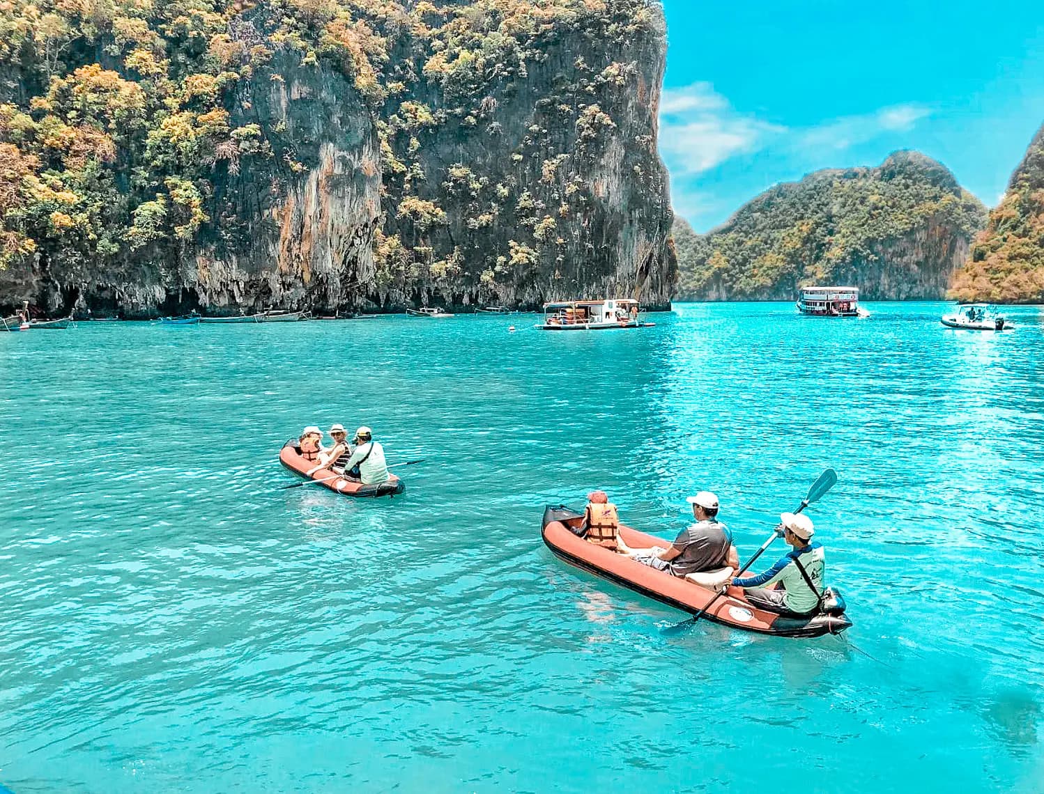 Guests paddling red inflatable sea canoes across turquoise water among limestone cliffs in Thailand