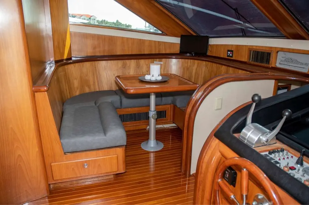 Wooden helm with wheel and throttles beside a gray dinette inside the motor yacht