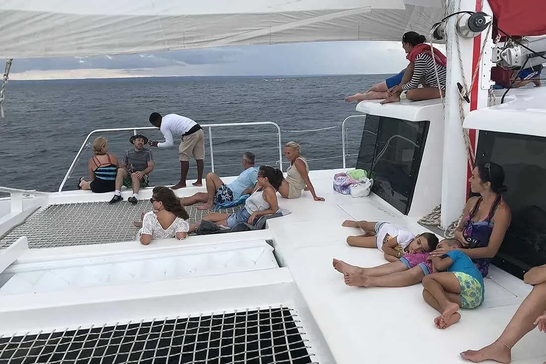 Woman resting with two kids on a sailing catamaran's foredeck as other guests relax by the bow nets
