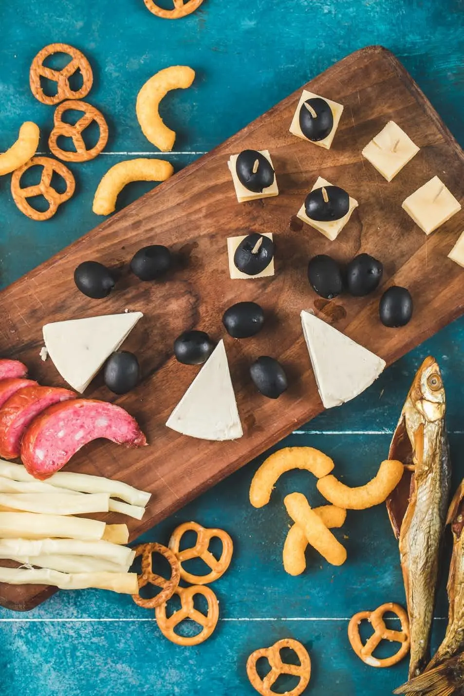 Snack board of cheese, olives, salami and pretzels on a blue wooden table