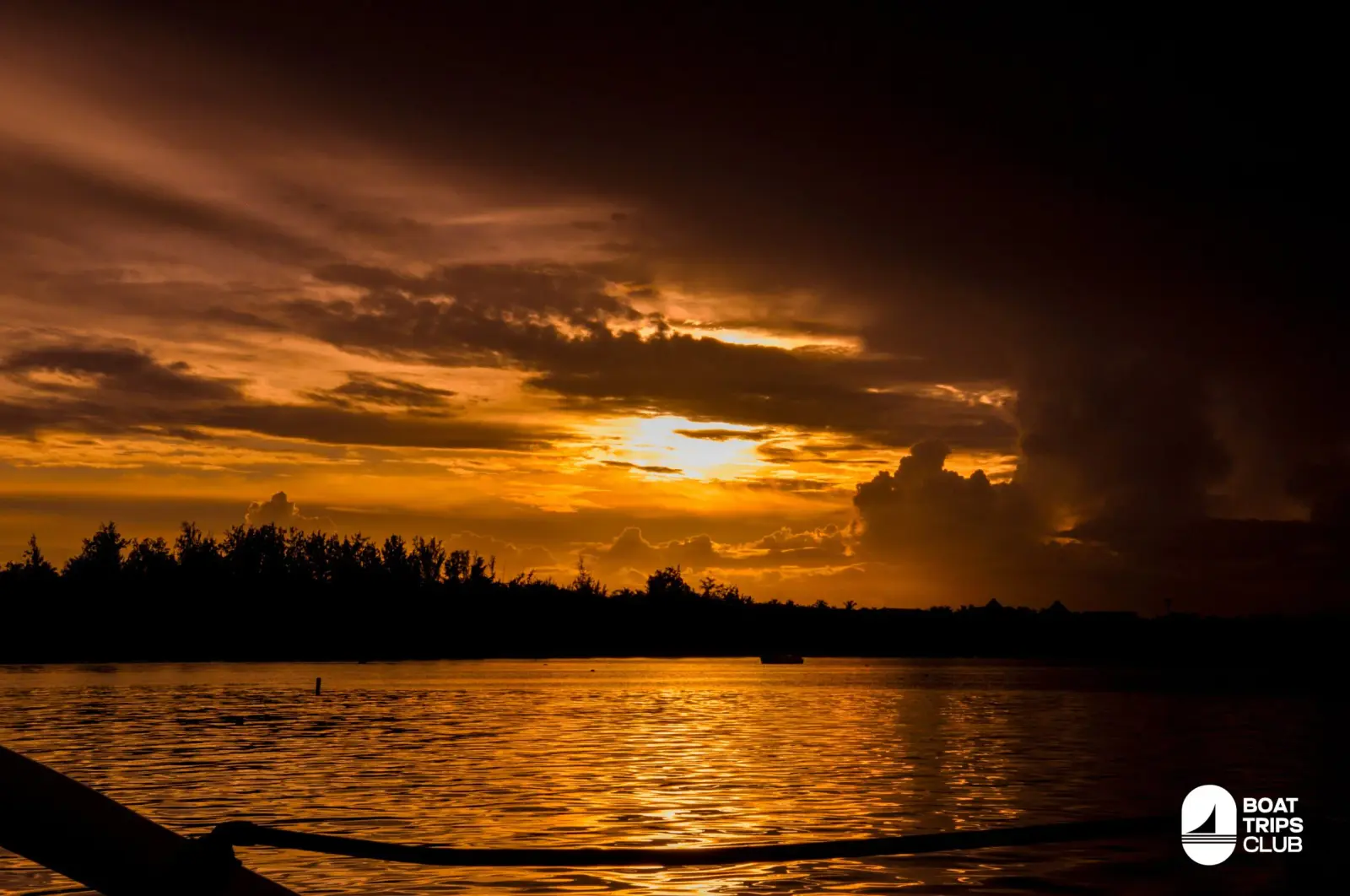 Amber sunset breaking through storm clouds over the dark Punta Cana shoreline, seen from a catamaran