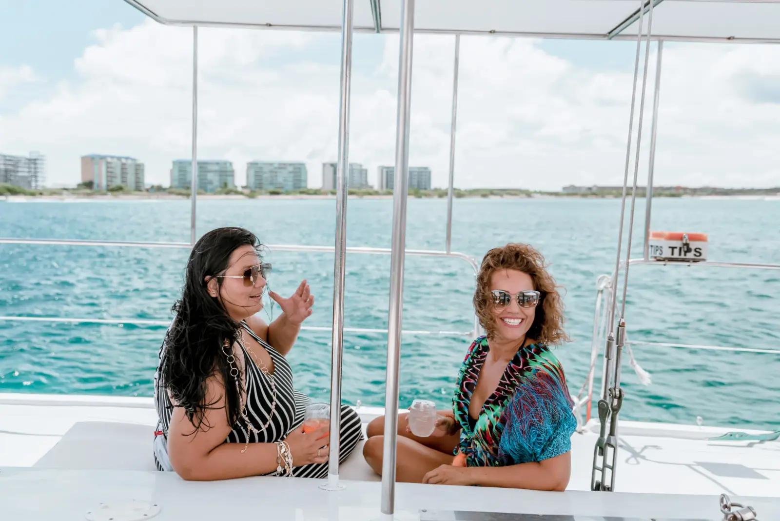 Two women relaxing on a catamaran deck with Palm Beach high-rise hotels across the water