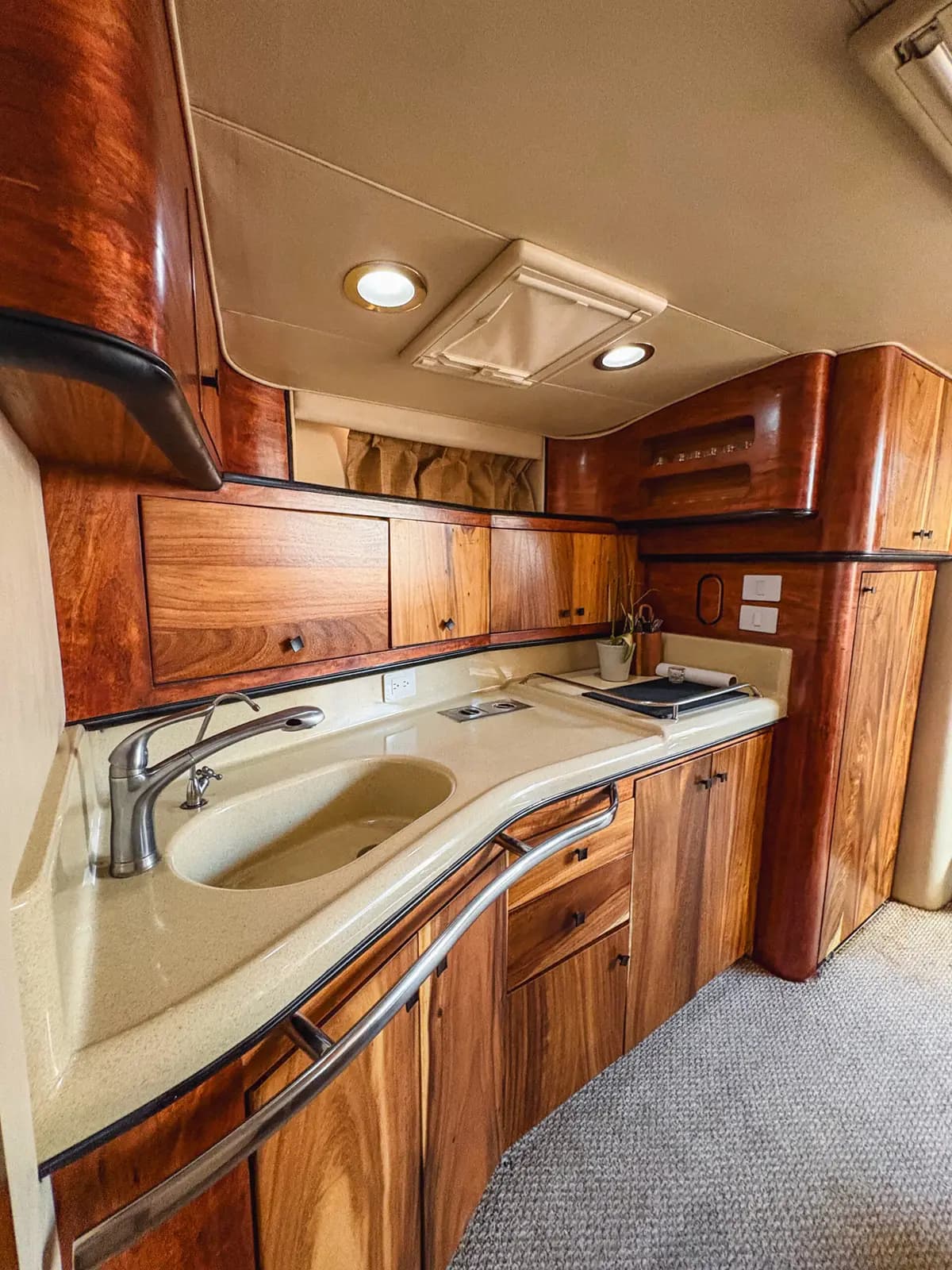 Yacht galley with a curved cream counter, steel sink and wood cabinets below deck