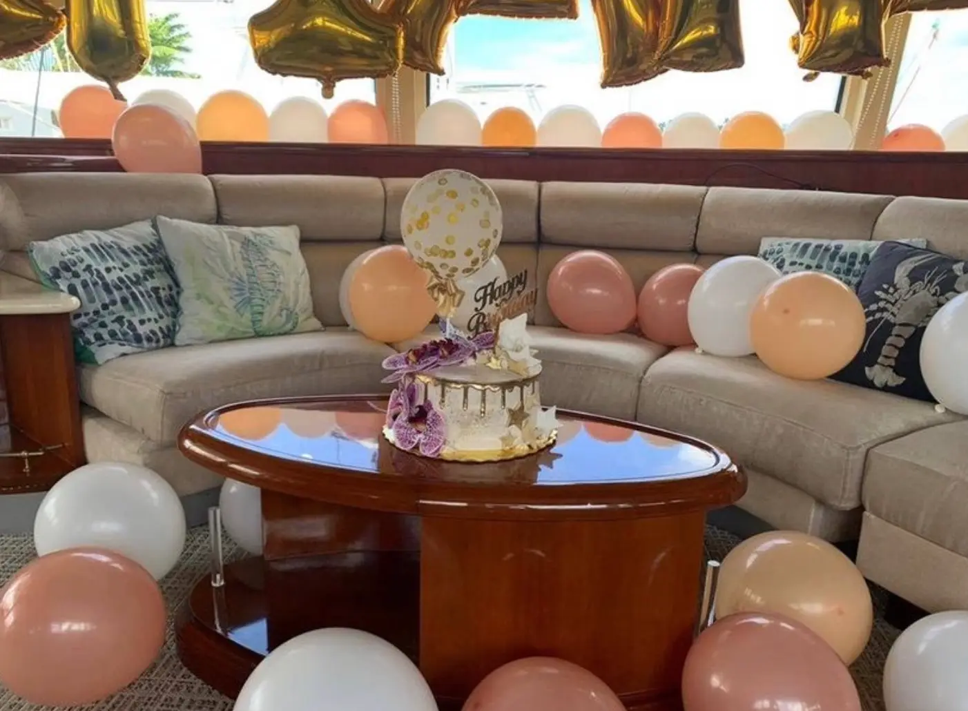 Yacht salon set for a birthday with pastel balloons and a decorated cake on the wooden table