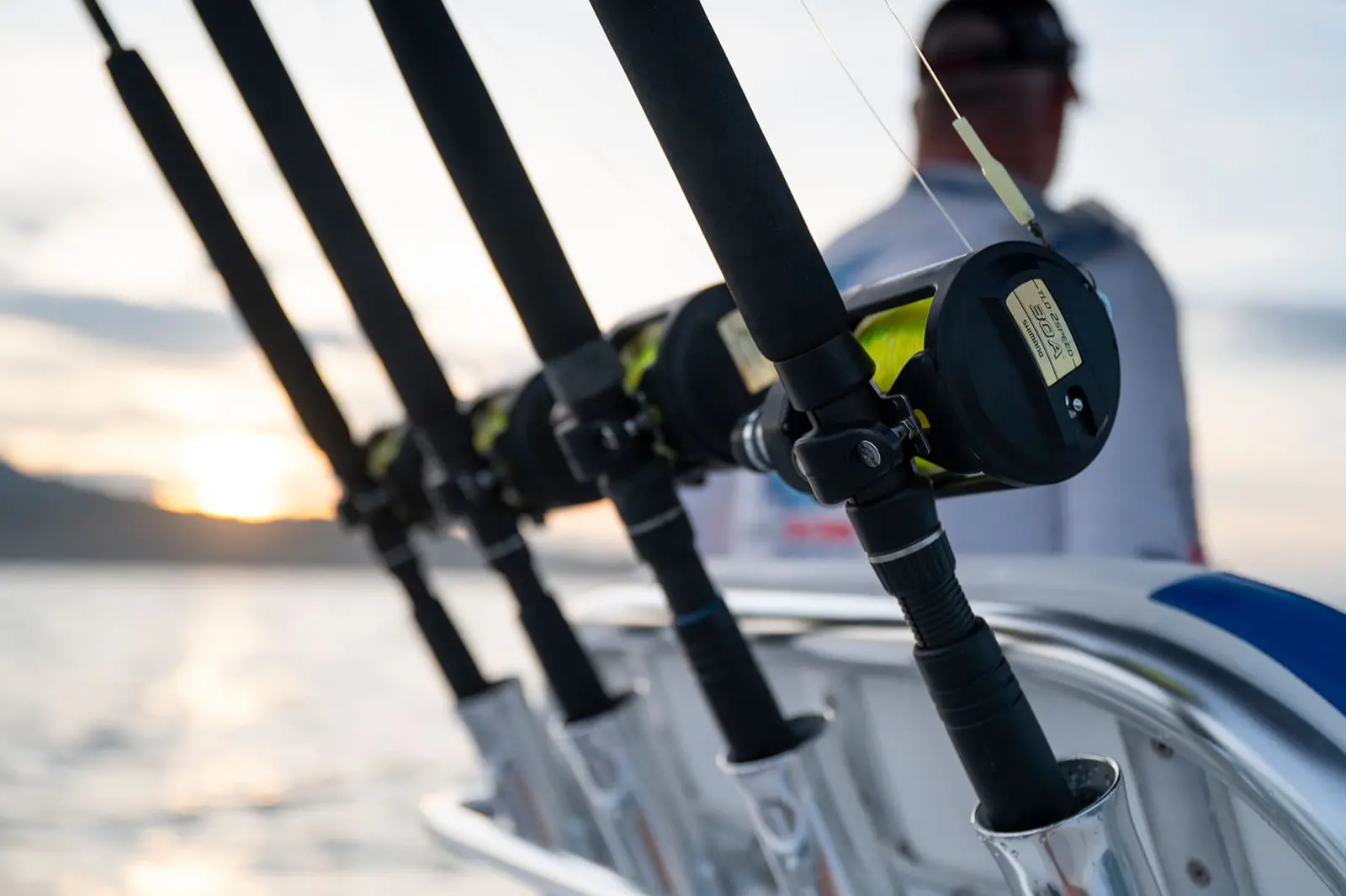 Row of fishing rods and reels in rod holders on a center console boat as the sun sits low over the water
