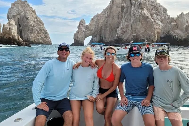 Five guests pose on the yacht's bow in front of the rock arch at Los Cabos