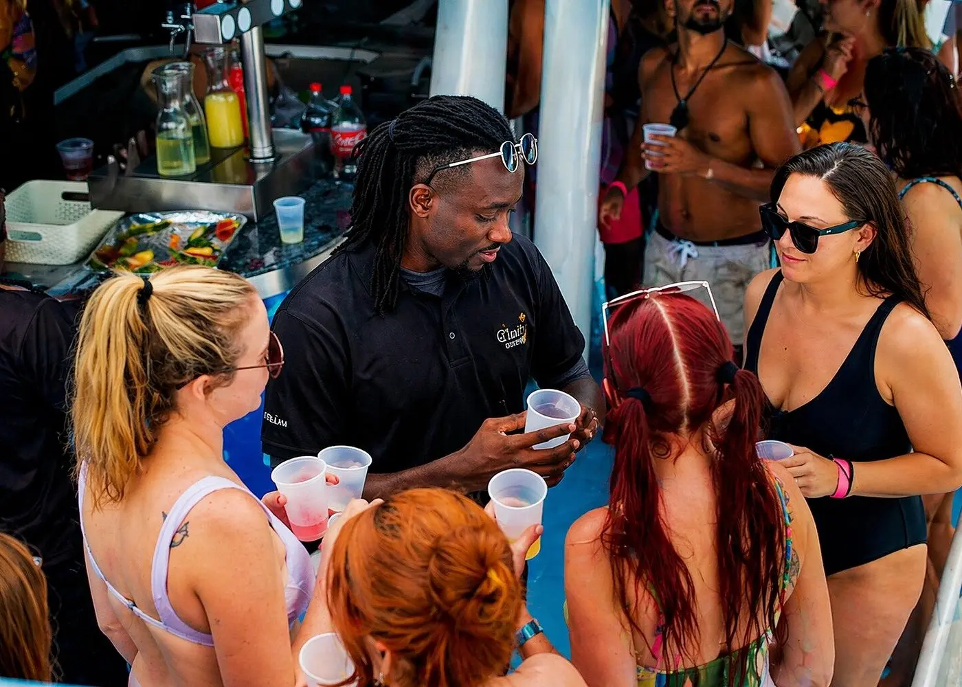 Crew bartender in a black polo handing out drinks to guests at the catamaran's onboard bar
