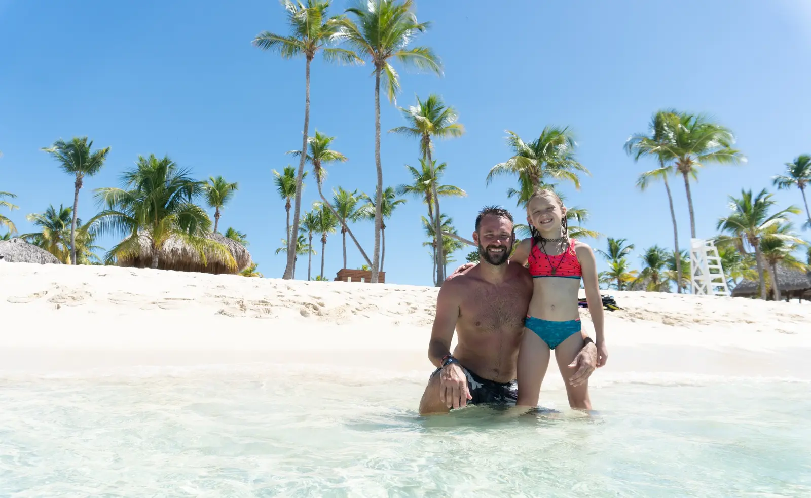 Man and a girl posing in the shallows of a palm-lined white-sand beach on Saona Island